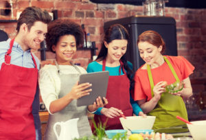 cooking class, friendship, food, technology and people concept - happy friends with tablet pc computer in kitchen